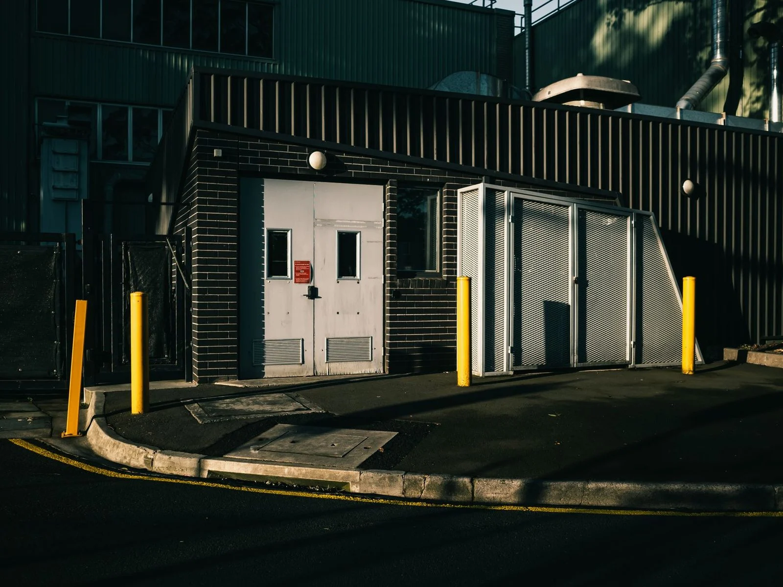 Entrada de un edificio industrial con puertas metálicas y bolardos de hormigón a lo largo del acceso.