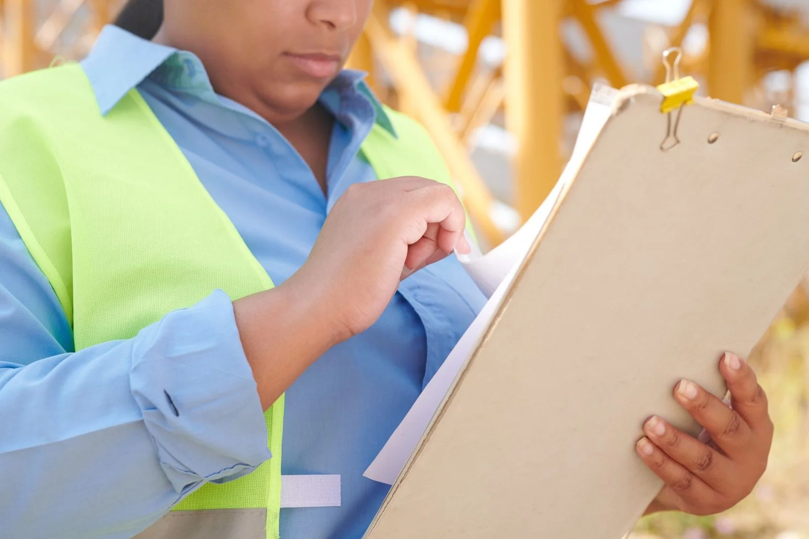 Ingeniera con casco y chaleco de seguridad revisando documentos en una tablilla en una obra de construcción.
