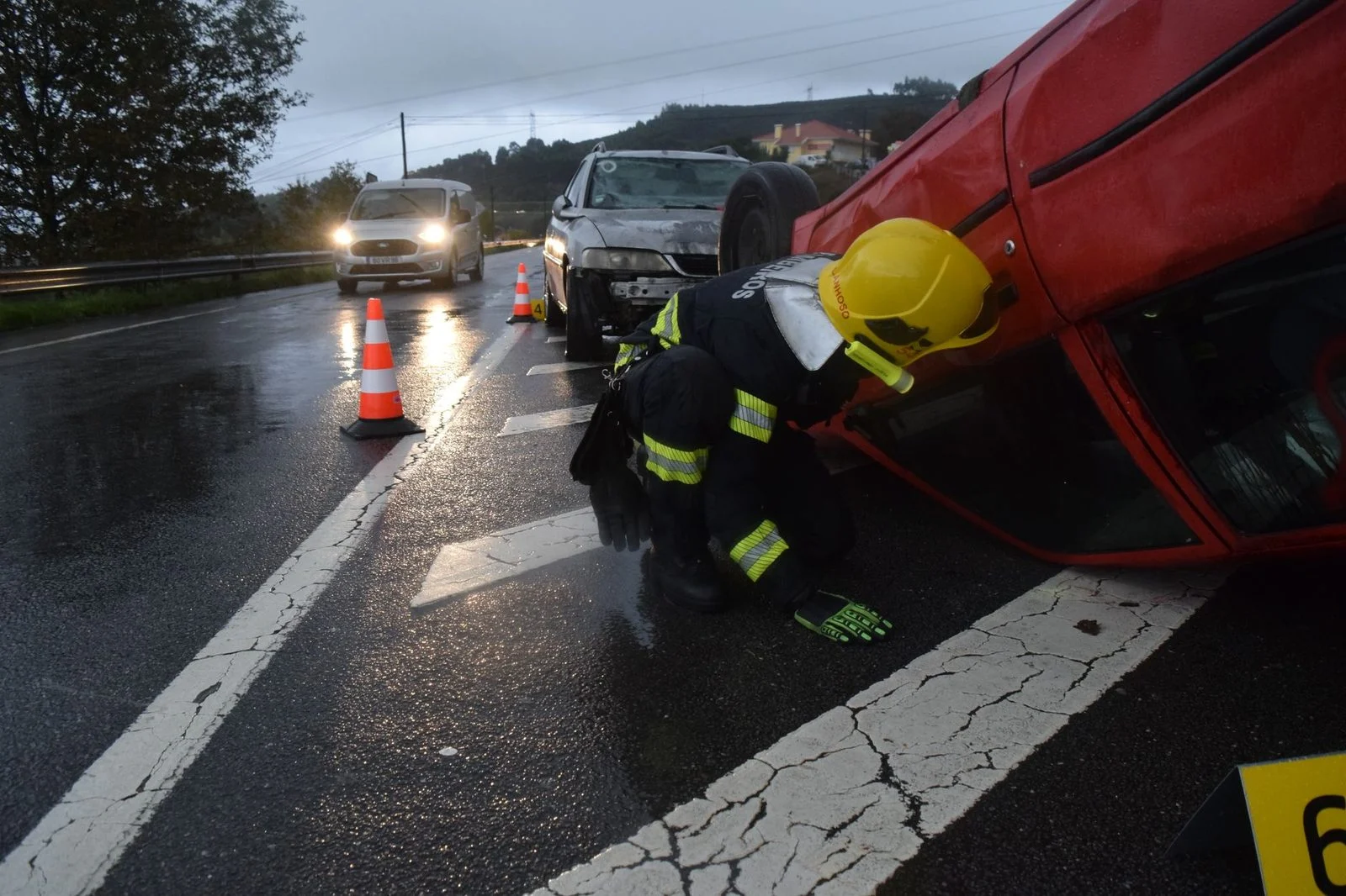 Firefighter assisting at overturned vehicle accident scene on wet road.