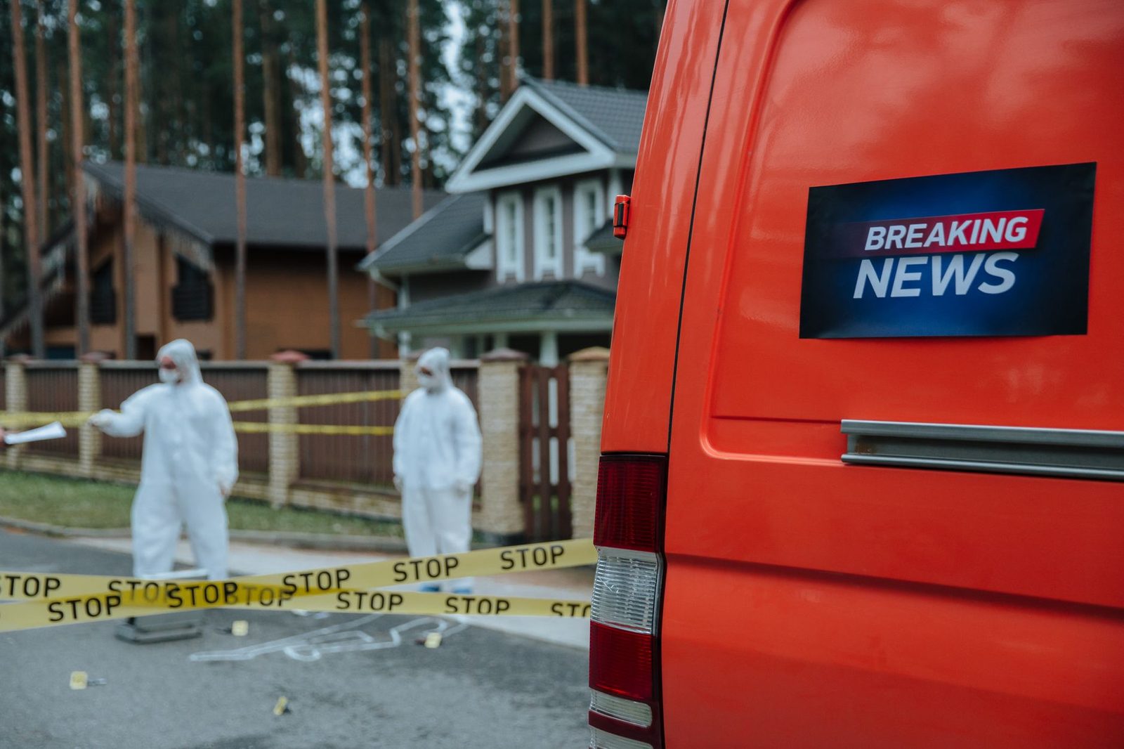 Forensic investigators in protective suits work at a marked-off crime scene near concrete houses