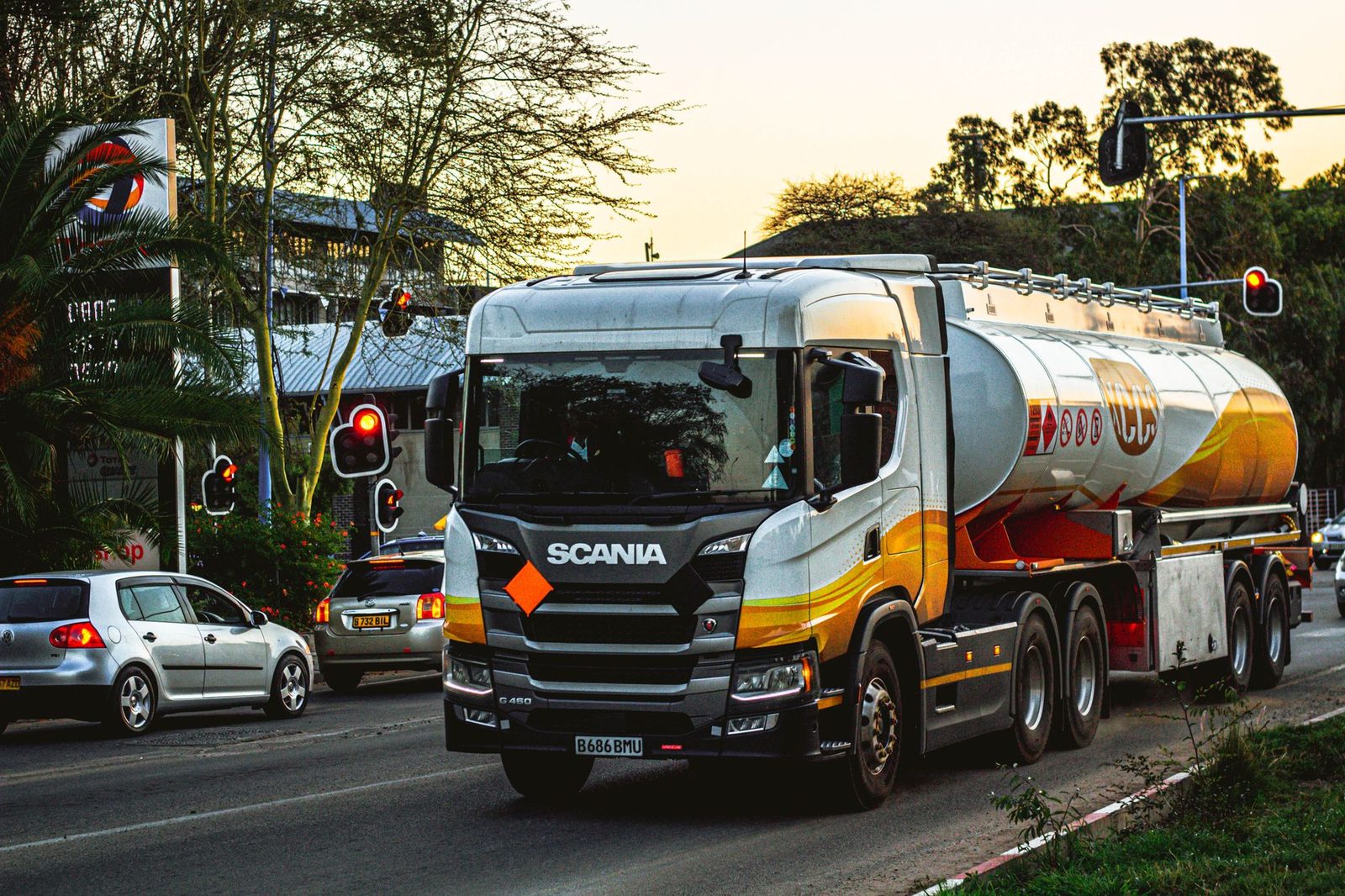 Camión cisterna de combustible circulando por una calle urbana a plena luz del día, rodeado de semáforos y vehículos.