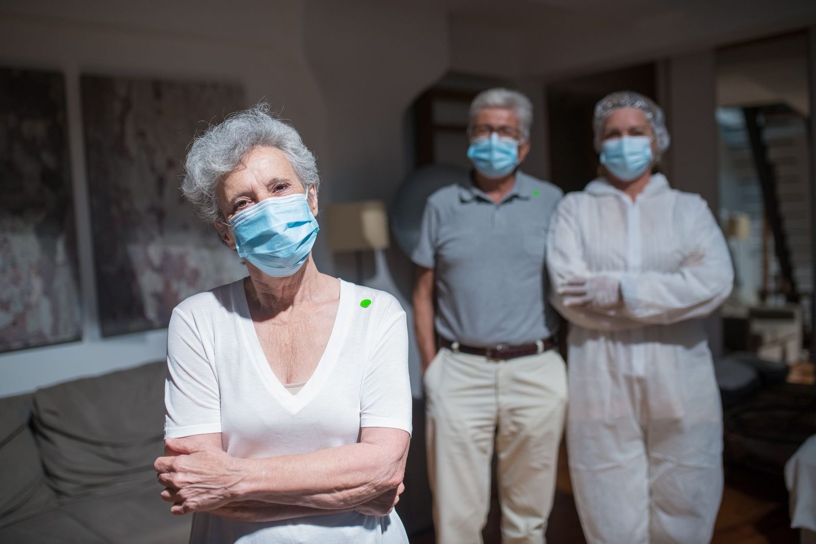 Healthcare workers in protective gear help elderly residents indoors during COVID-19 care.