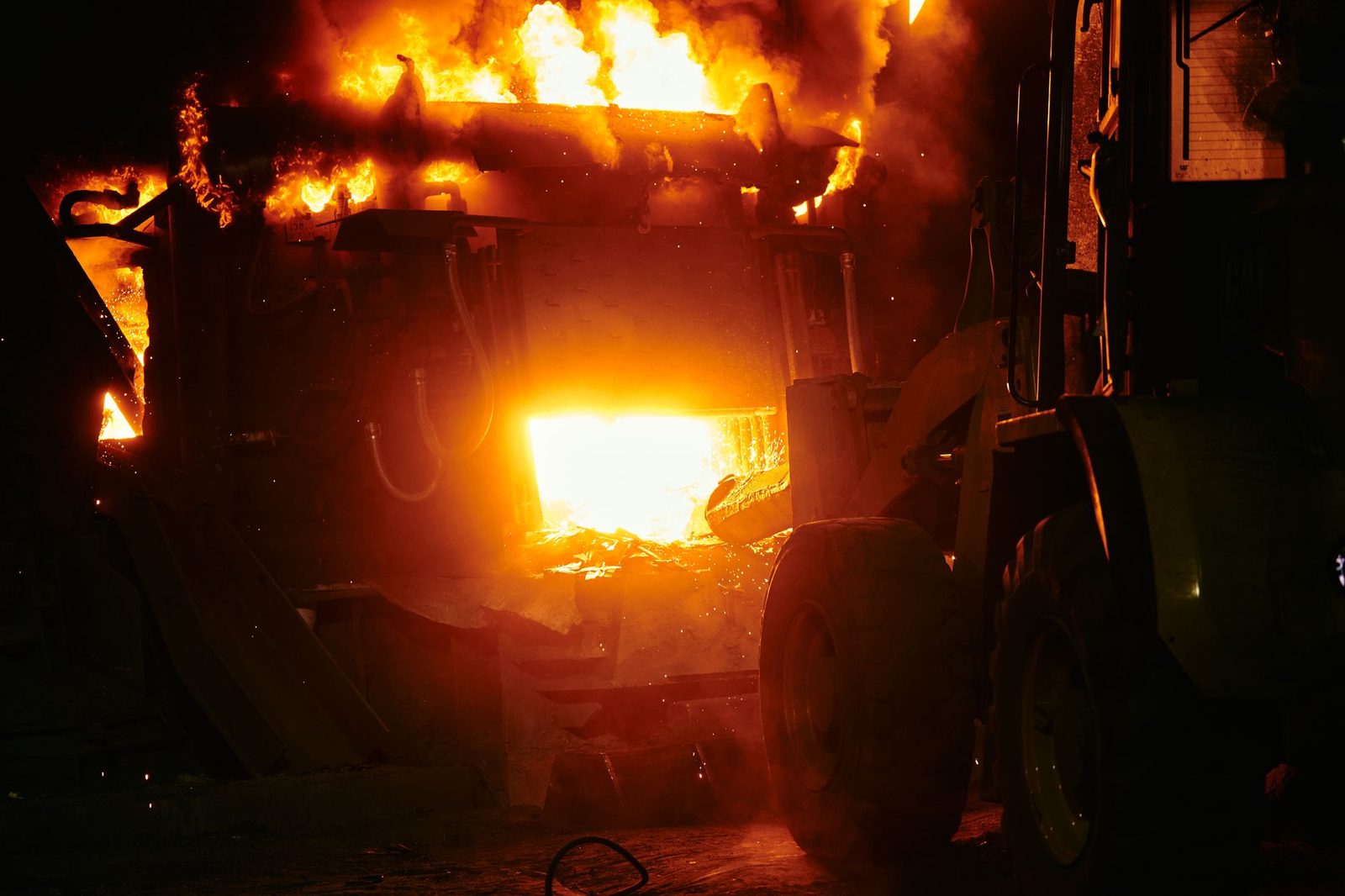 Industrial fire with flames engulfing machinery at night.