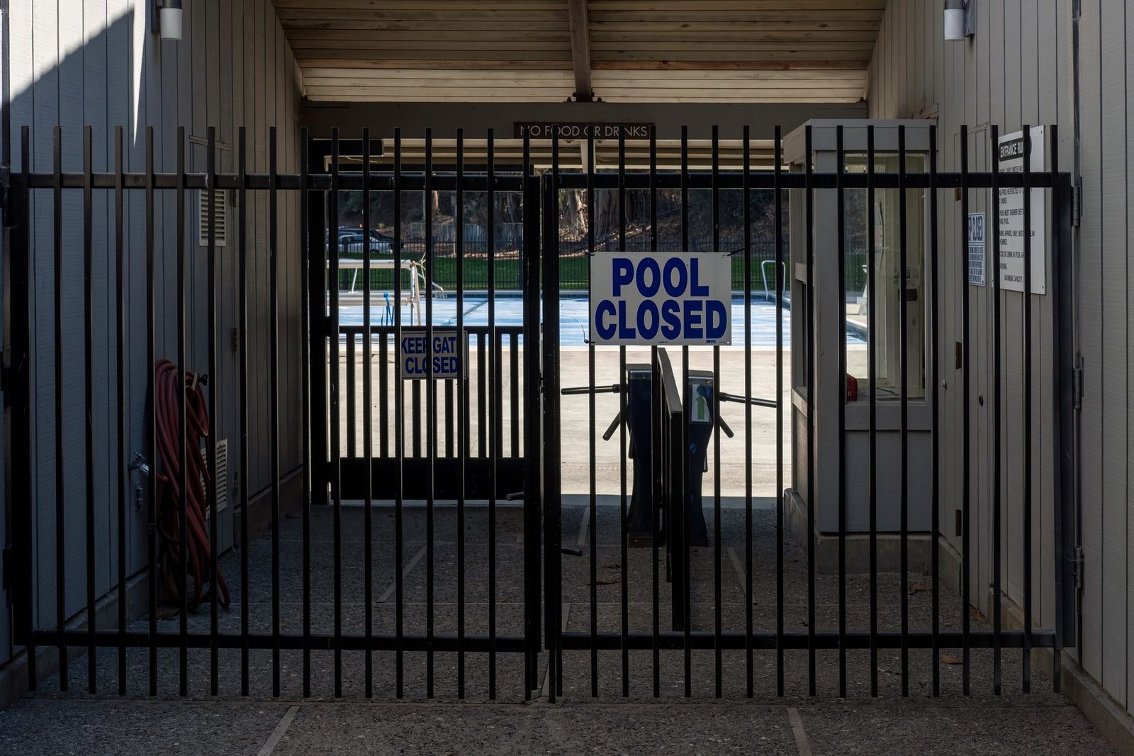 Puerta de hierro forjado cerrada con candado en la entrada de una piscina comunitaria, con un letrero visible.