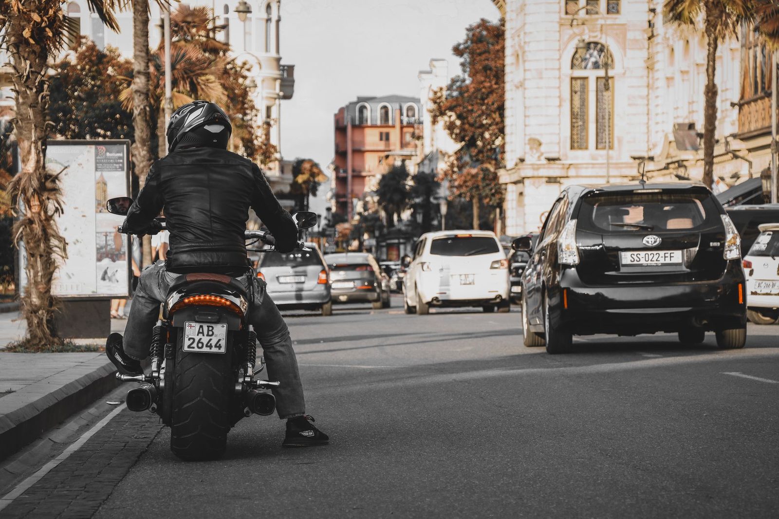 Motociclista en chaqueta de cuero conduciendo por calle urbana con edificios históricos.