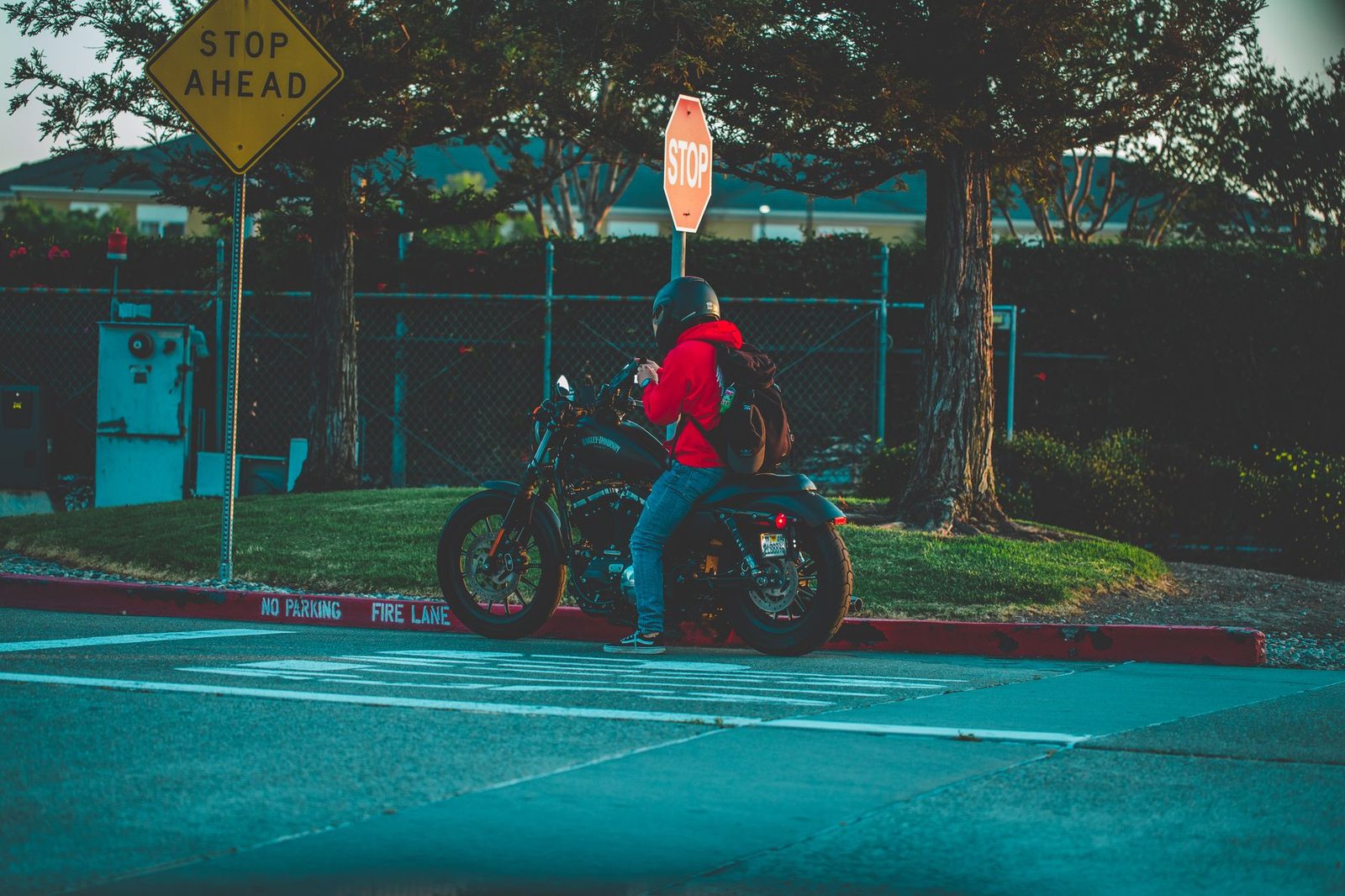 Motorcyclist in red jacket stopped at urban intersection observing traffic.