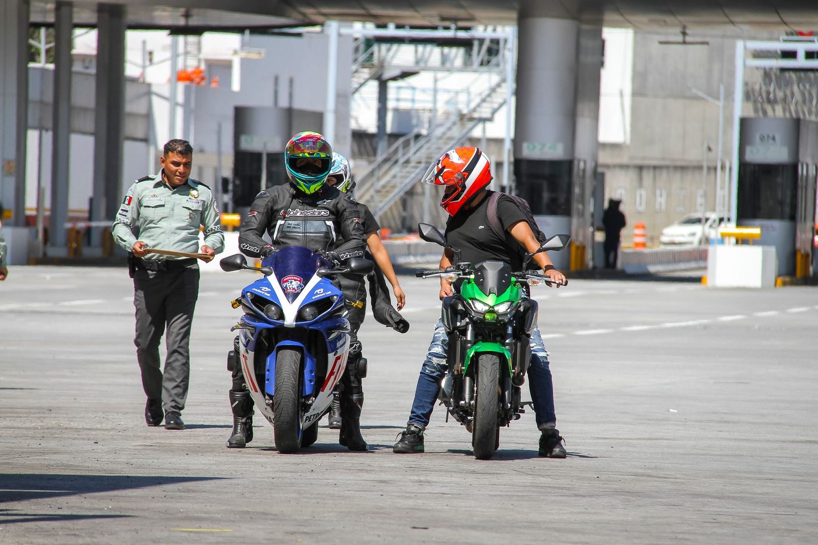 Motociclistas con casco conversan con un agente de policía en un punto de control al aire libre.