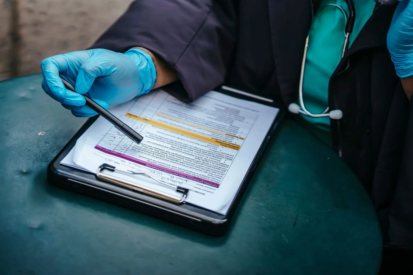 Overhead view of a doctor in disposable gloves writing on a paper clipboard at a table.