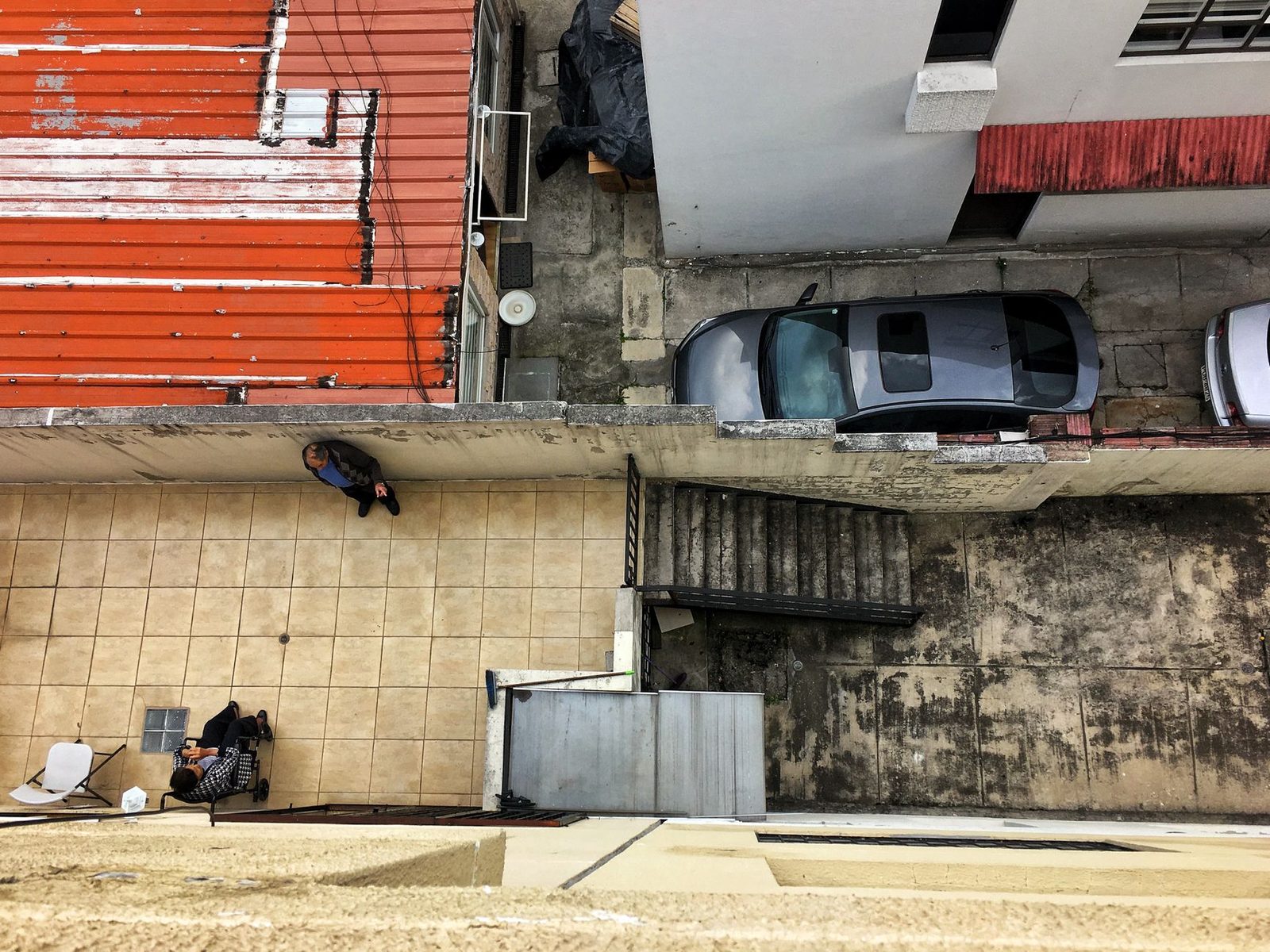 Patio urbano desde arriba con dos personas y autos estacionados.