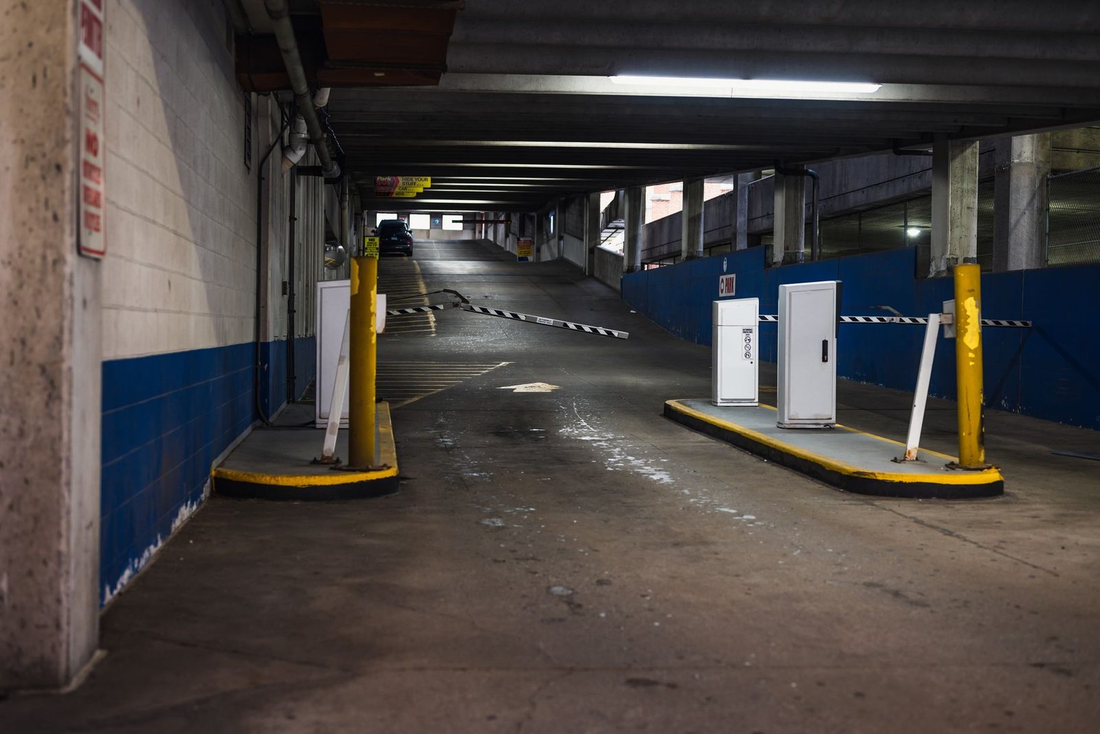 Rampa de entrada a estacionamiento subterráneo con barreras e iluminación tenue.