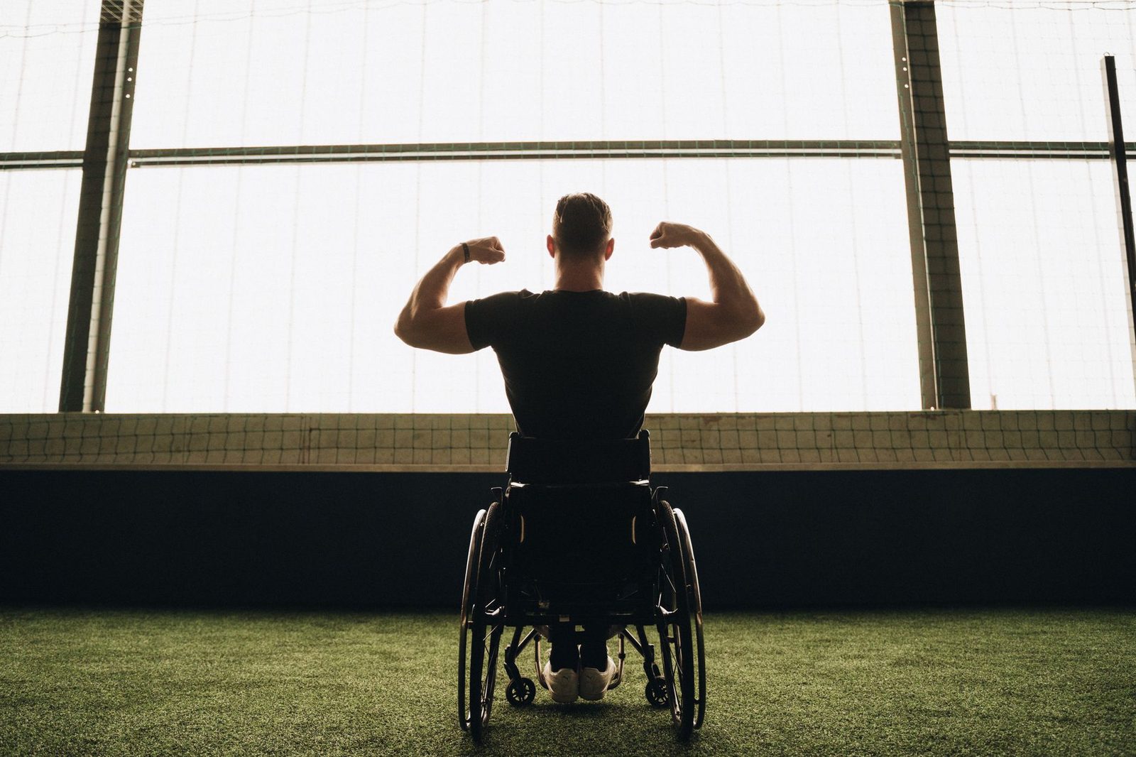 Hombre musculoso en silla de ruedas, de espaldas, flexionando los brazos en un gimnasio deportivo.