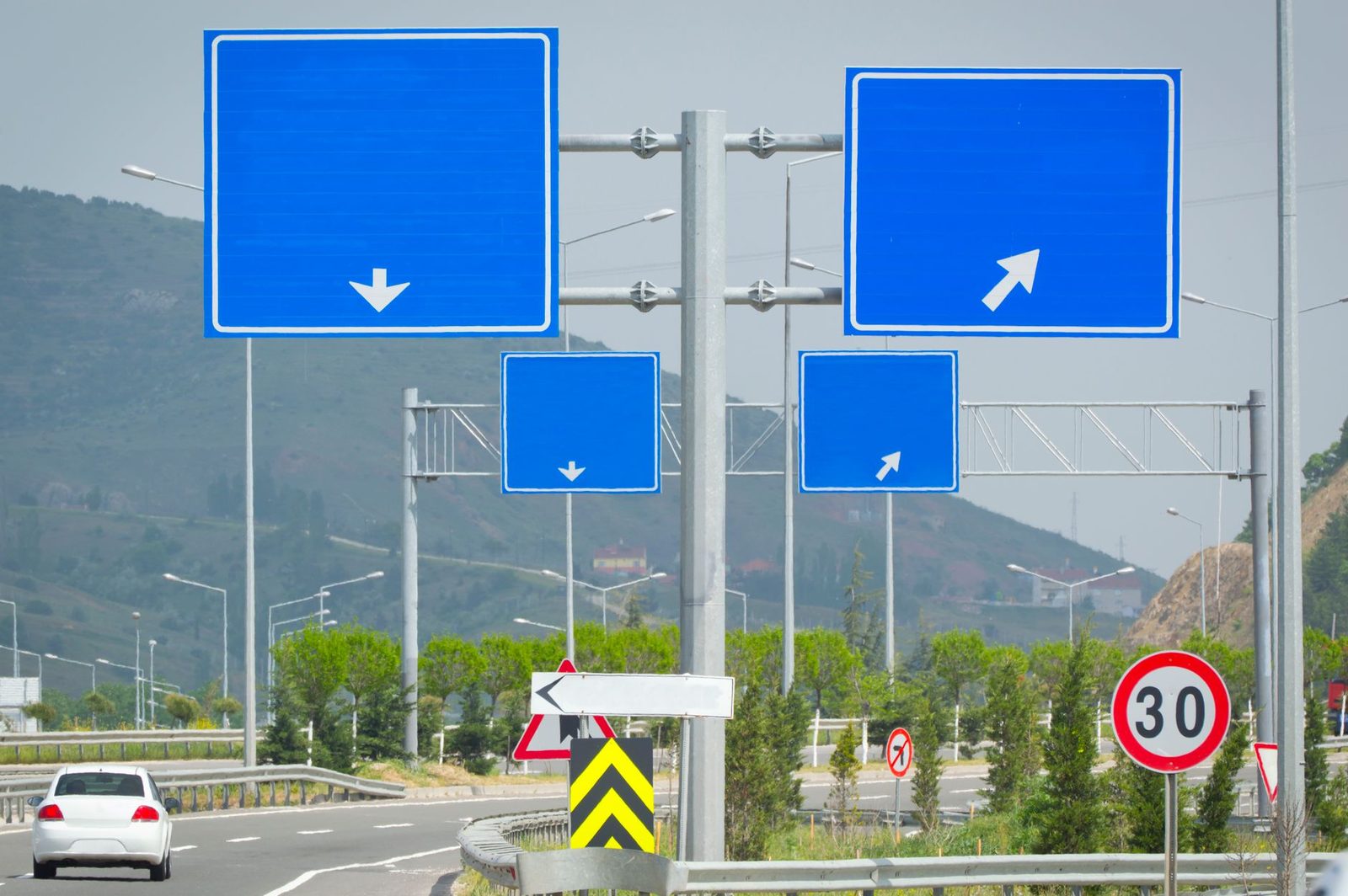 Series of blank blue road signs with arrows on a highway intersection and speed limit in scenic outdoor setting.