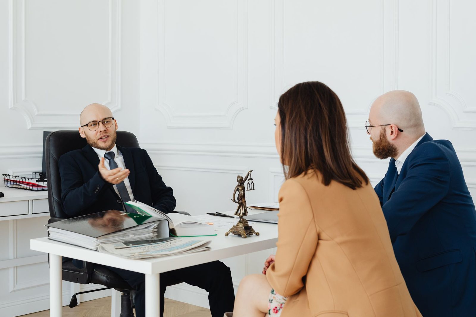 Tres adultos sentados en una mesa de conferencias revisando documentos legales durante una reunión de trabajo.