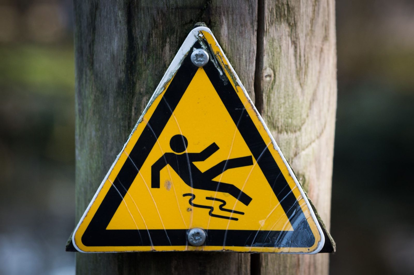 Close-up of a yellow triangular wet floor warning sign on a wooden post.