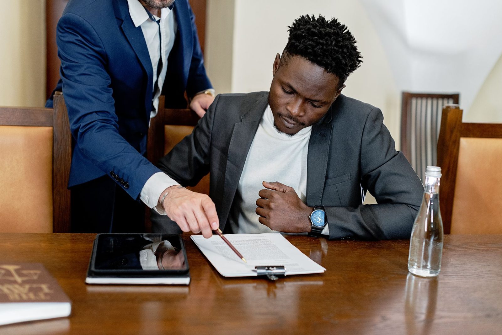 Two businessmen review a document and tablet together during a legal consultation at a desk.