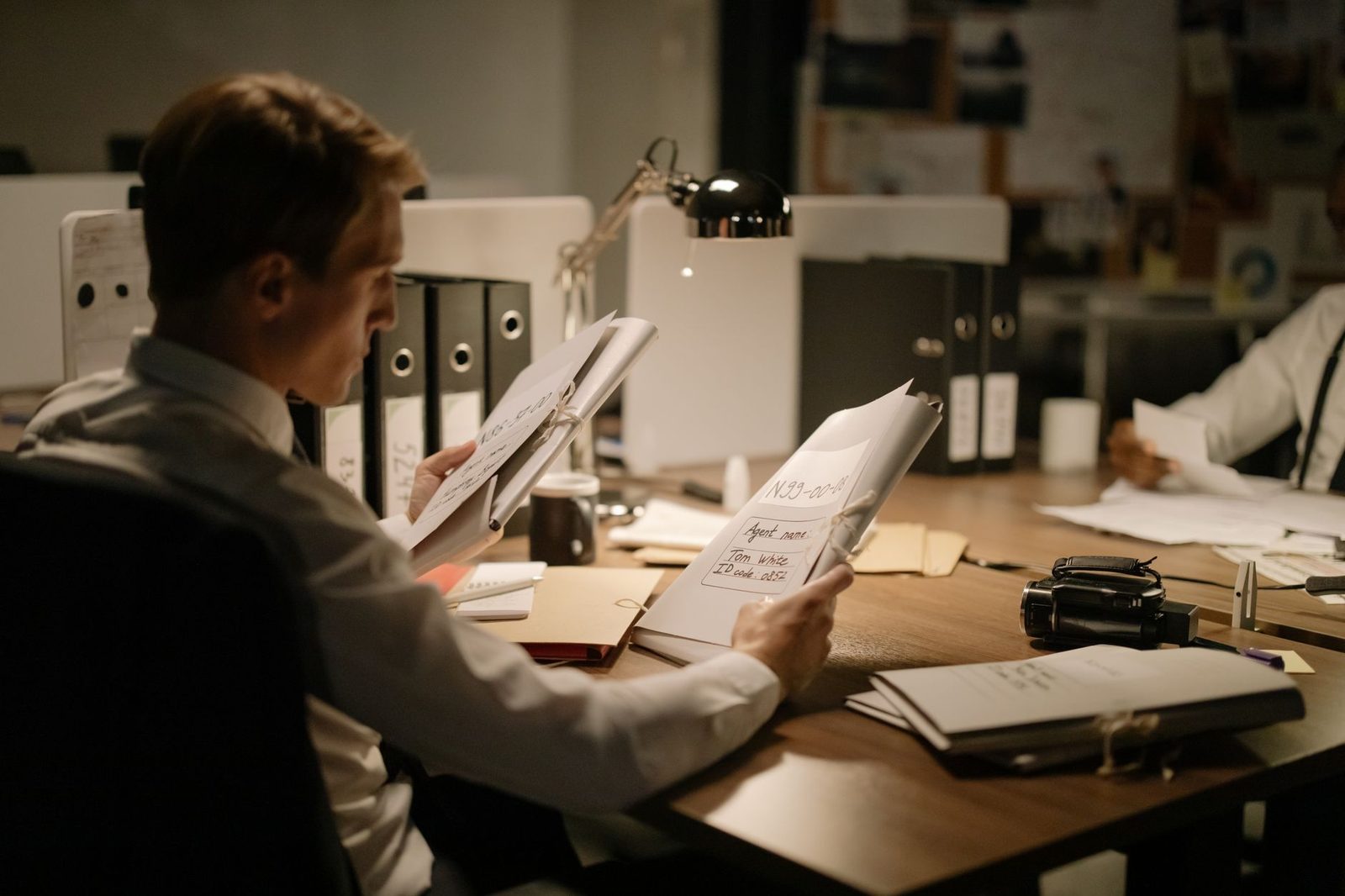 Two detectives in a dim office closely review case documents together.