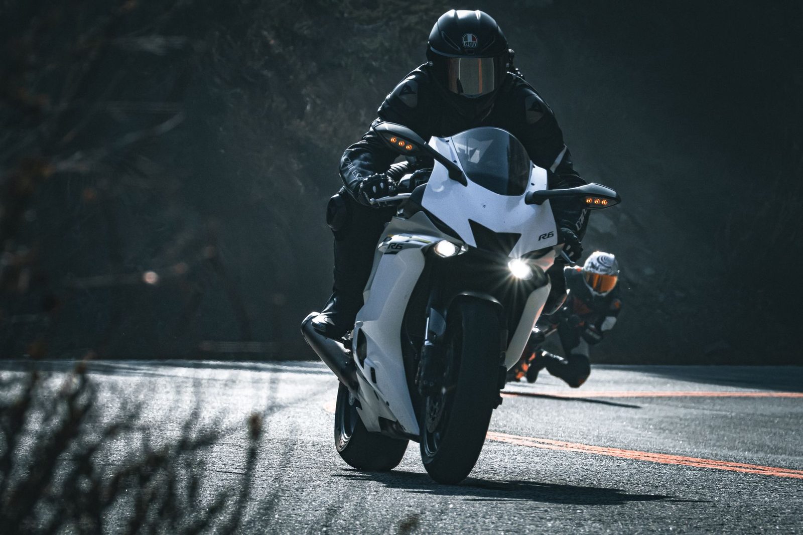 Two motorcyclists riding on a curved road demonstrating proper spacing and control techniques.