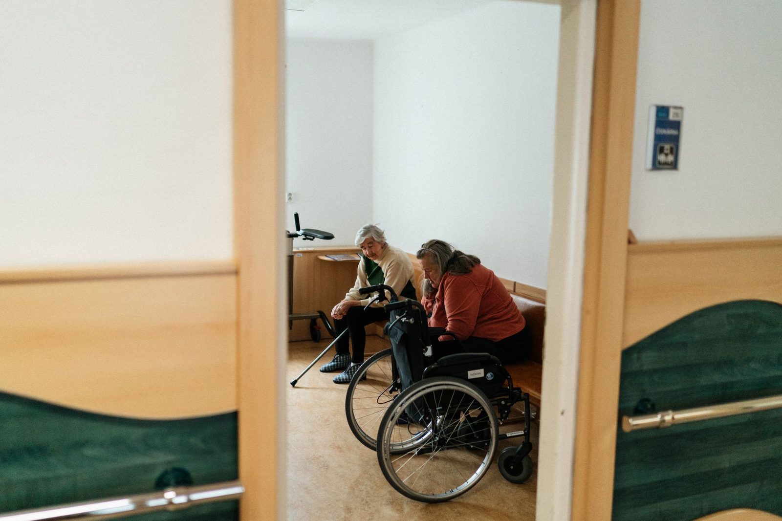 Dos mujeres mayores conversan en el interior, una de ellas sentada en silla de ruedas.
