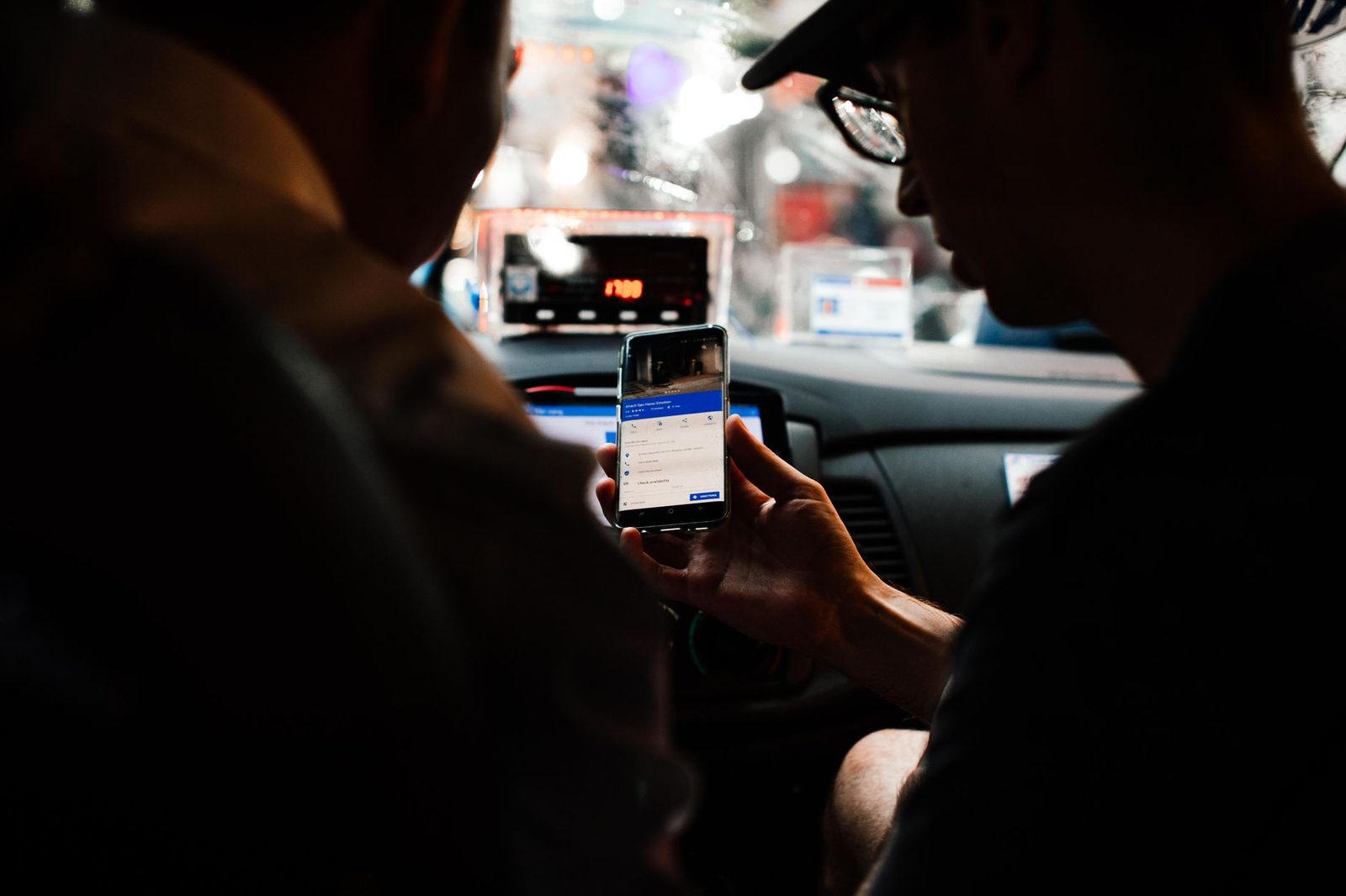 Two people look at a smartphone for directions while sitting in a car at night.