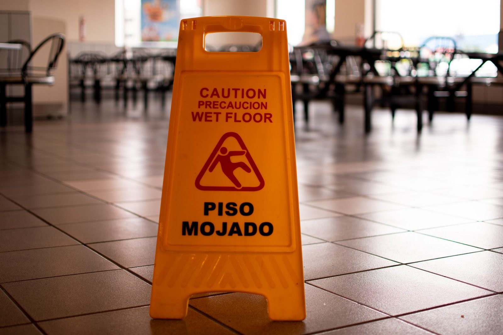 Letrero amarillo de "piso mojado" sobre un suelo de baldosas en una cafetería.